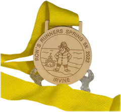 Round wooden bespoke medal engraved with a lifeguard and sandcastle design on a yellow ribbon