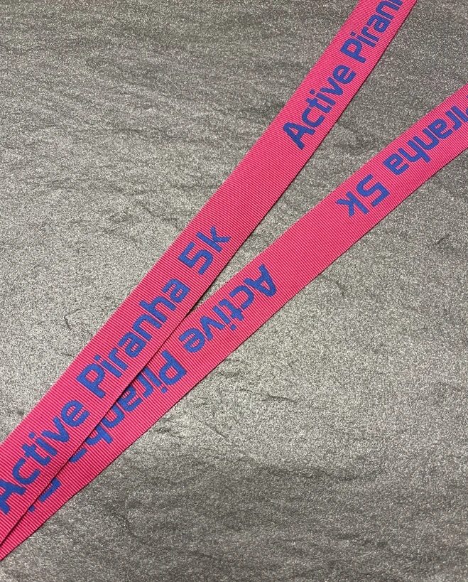 Active Piranha 5k printed in blue on a pink woven ribbon